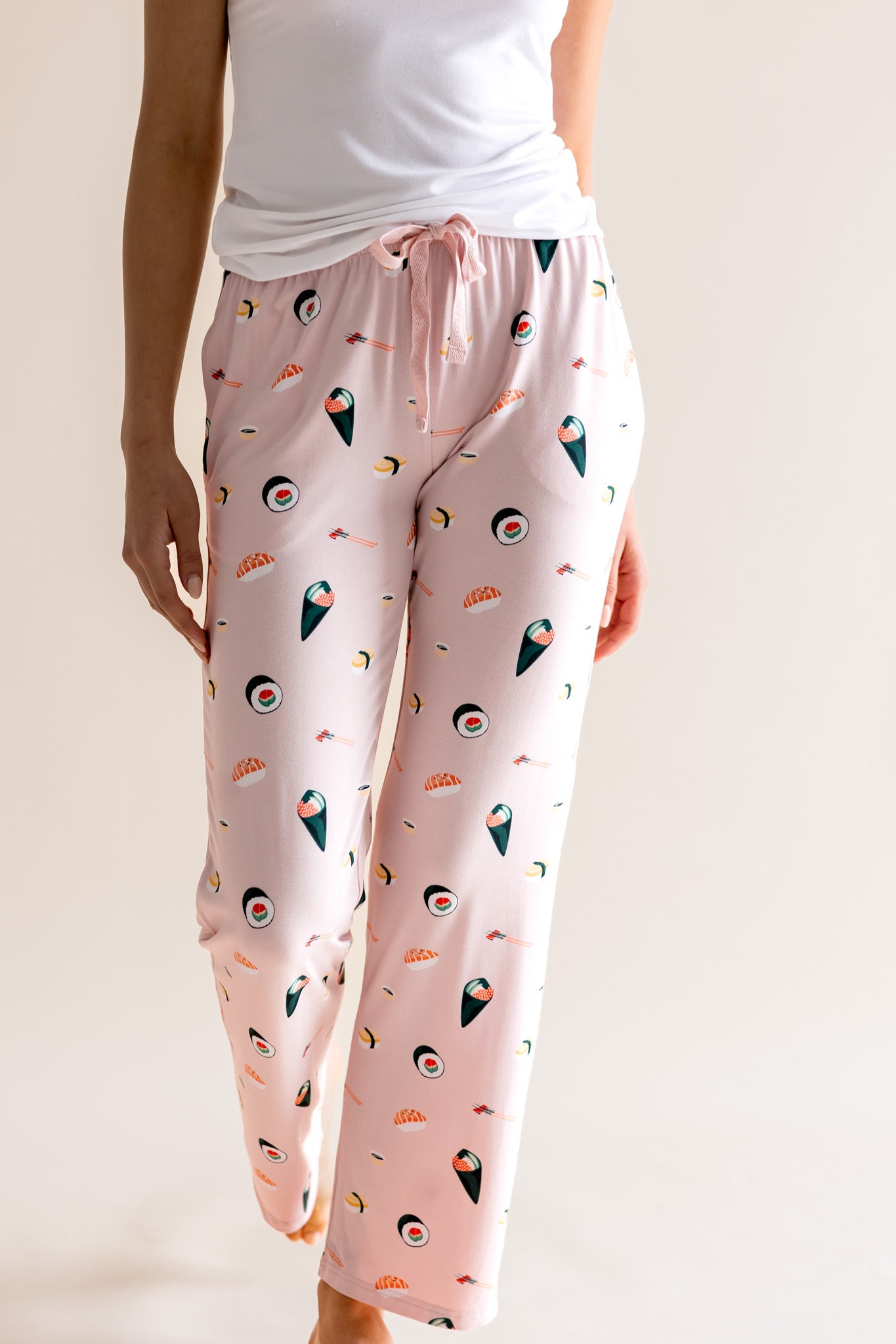 Model wearing pink Women's Lounge Pants in Sushi print under white camisole on a beige background