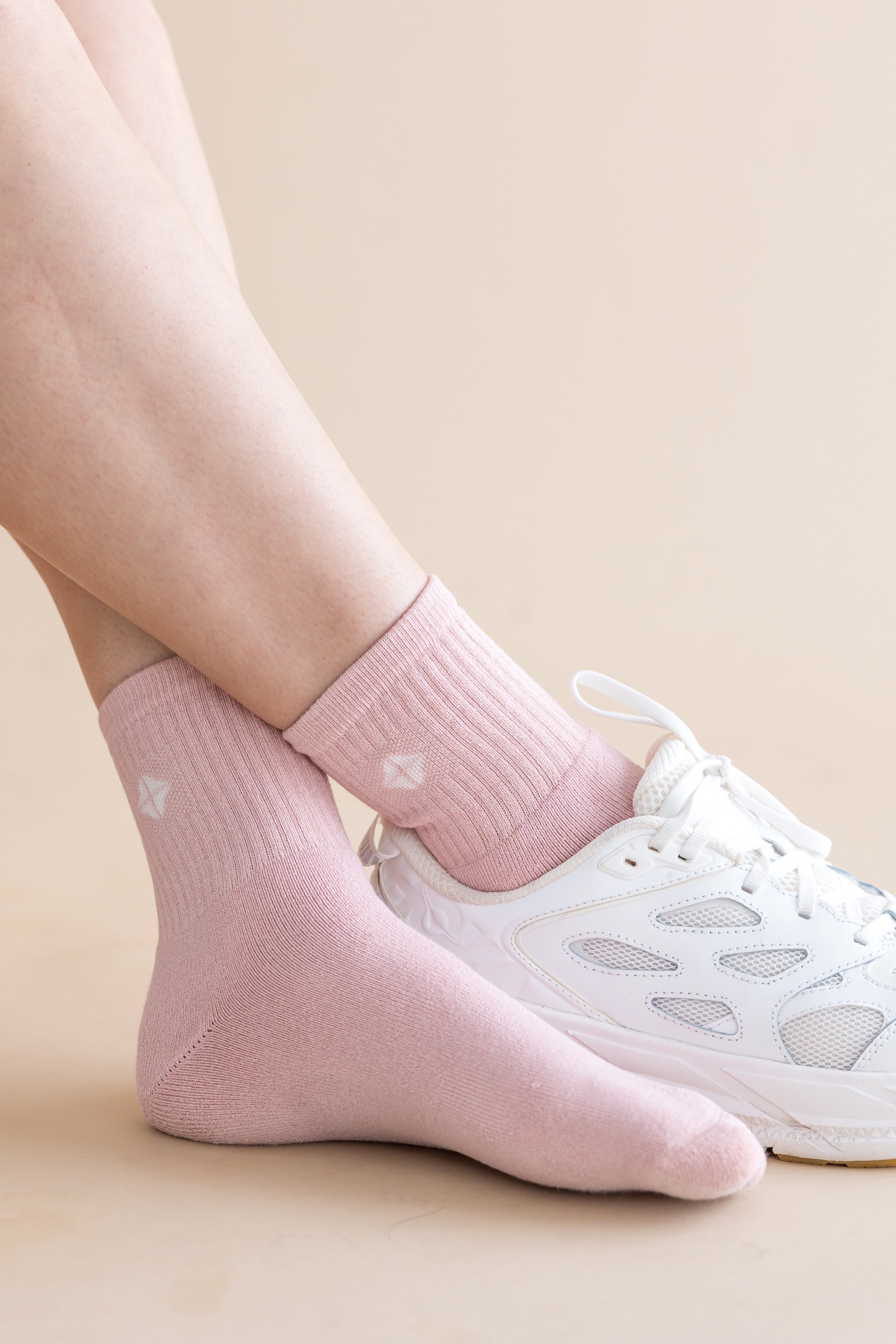 Pink socks with kite designs worn with white sneakers on a beige background
