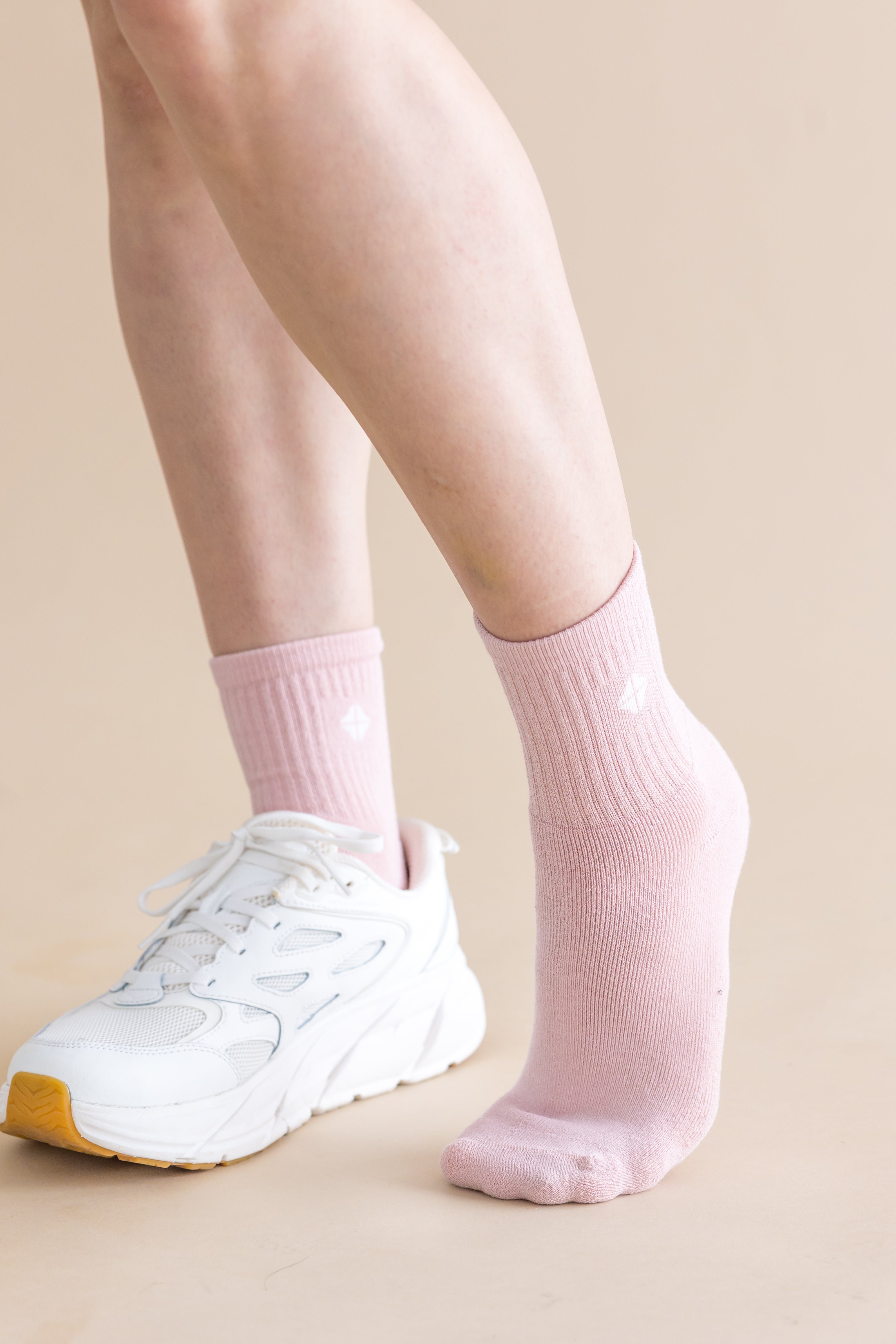 Person wearing pink socks and white sneakers on a beige background