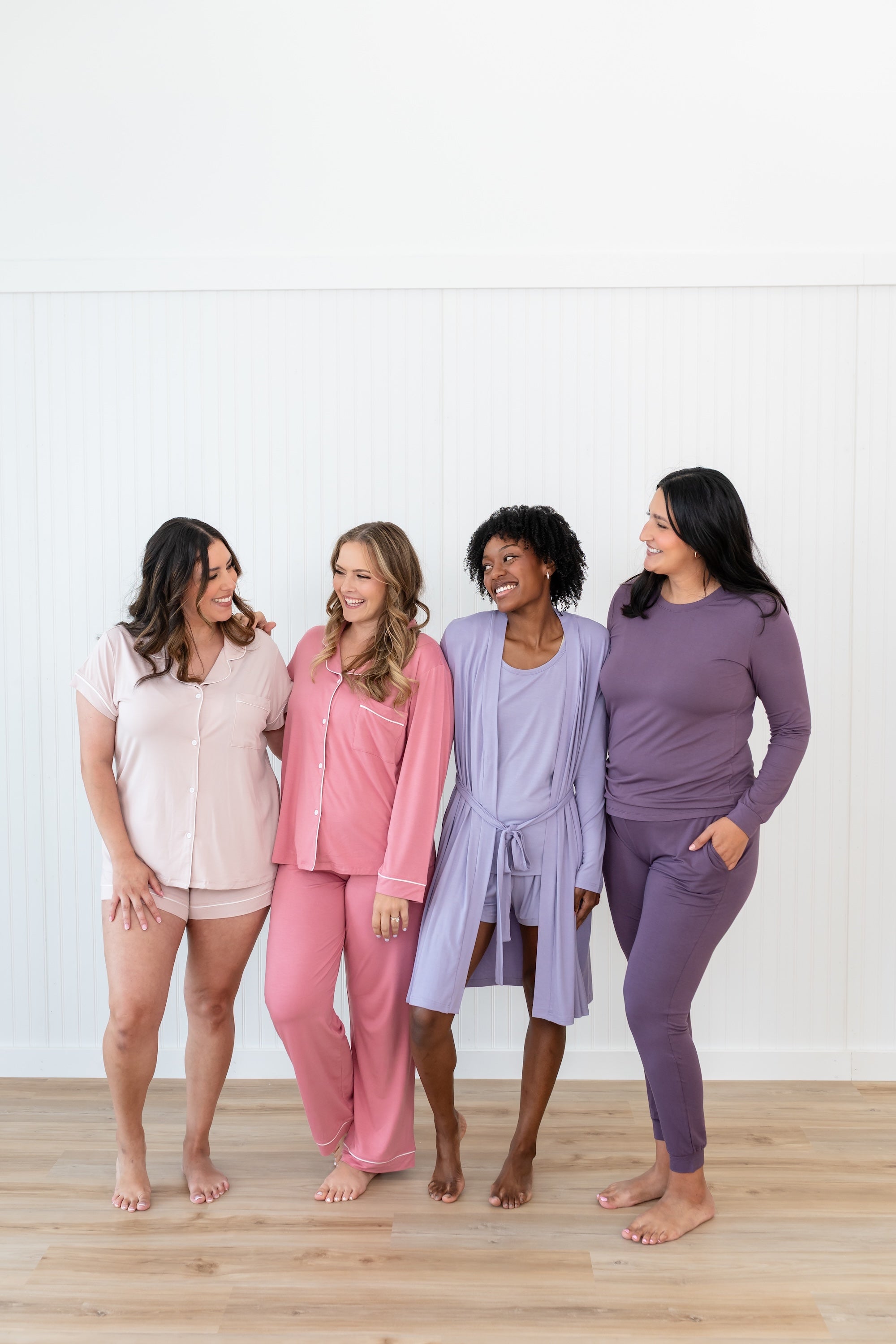 Group of 4 women modeling Kyte Living loungewear and pajamas in pink and purple hues