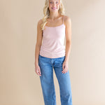 Woman wearing a pink tank top and blue jeans against a beige background