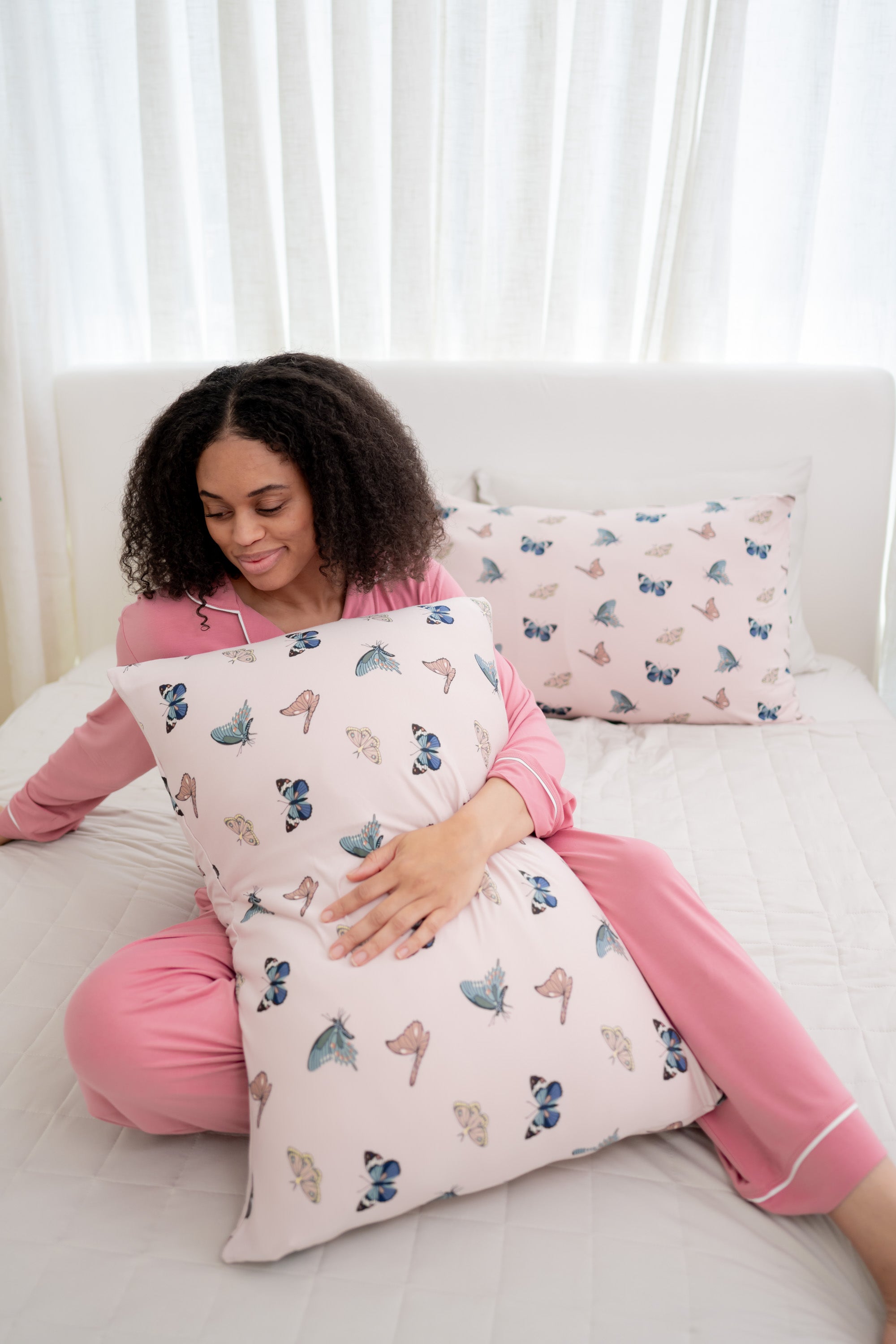 Woman in apple blossom pajamas modeling with Standard Pillowcase in Blush Butterfly on a bed 