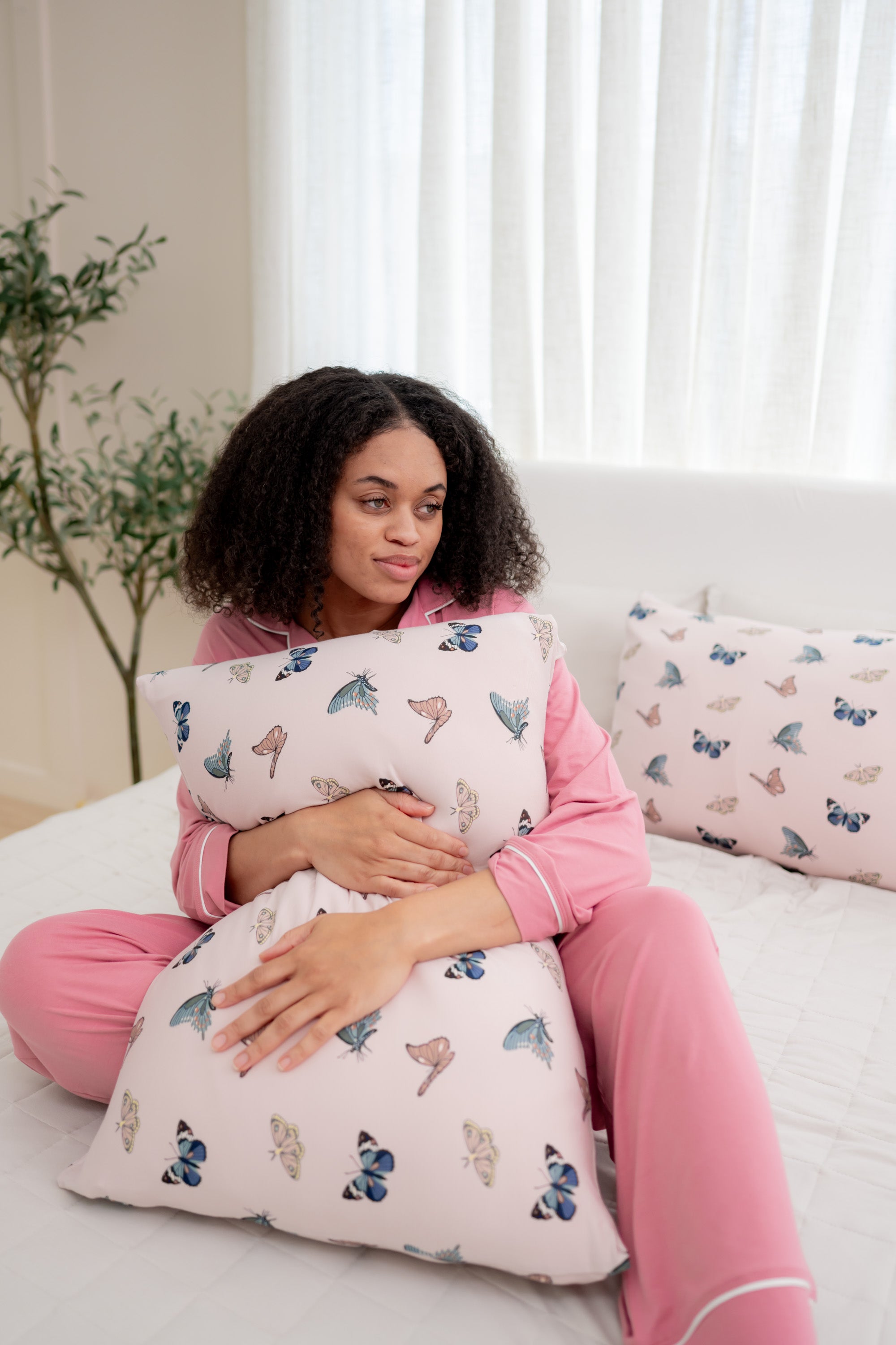 Woman in apple blossom pajamas modeling with Standard Pillowcase in Blush Butterfly on a bed 