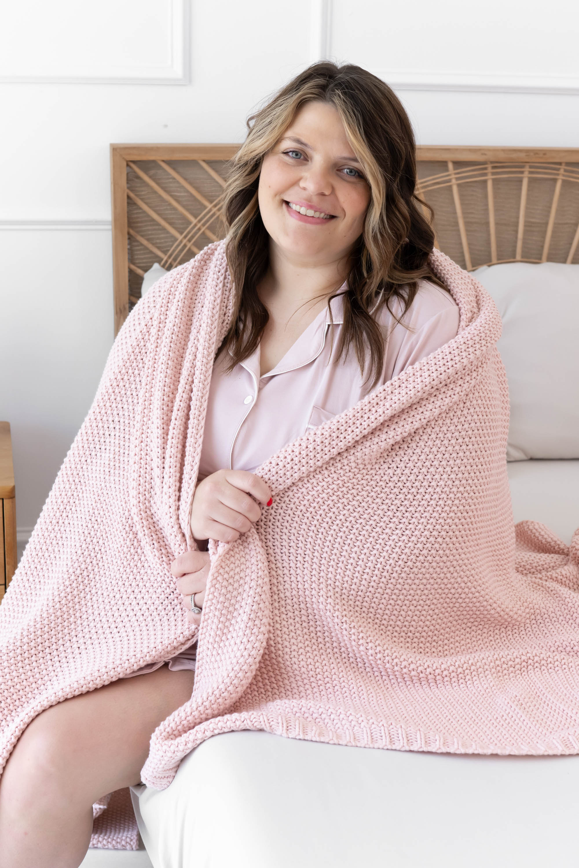 Model sitting in bed with the Chunky Knit Throw Blanket in Blush wrapped around her