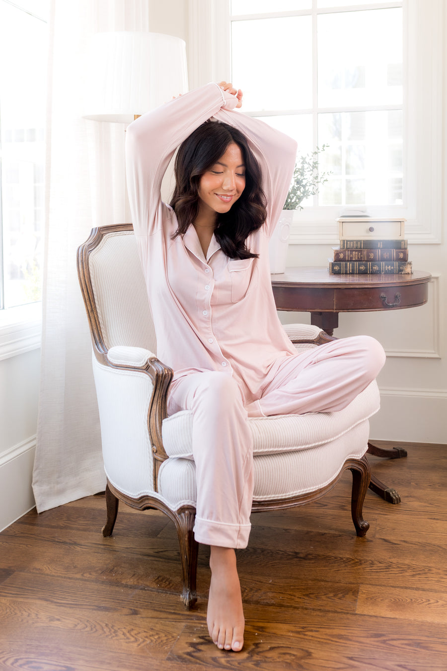 Woman in pink pajamas sitting on a white chair in a bright room.