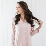Woman looking to the side with hand in hair while modeling the Kyte Long Sleeve Women's Pajama Set in Blush with Cloud Trim 
