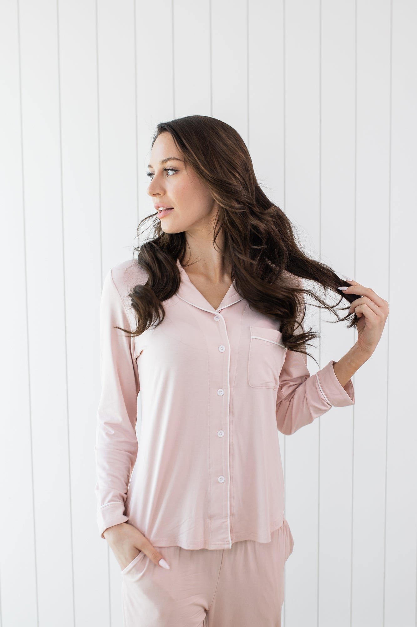 Woman looking to the side with hand in hair while modeling the Kyte Long Sleeve Women's Pajama Set in Blush with Cloud Trim 