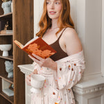 Modal holding a book wearing Women's Kimono Robe in Book Club print in a living room