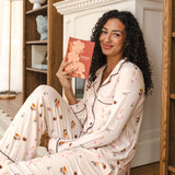 Modal wearing Long-Sleeved Women's Pajama Set in Book Club print sitting with a book in a living room