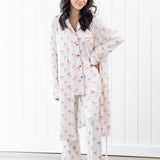 Woman wearing a white pajama set with pink bow patterns in a room with white walls and wooden floor.