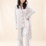 Woman wearing a white pajama set with pink bow pattern and matching robe on a beige background