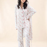 Woman wearing a white pajama set with pink bow pattern and matching robe on a beige background