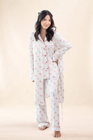 Woman wearing a white pajama set with pink bow pattern and matching robe on a beige background