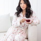 Woman in a white robe with pink bow pattern sitting on a white couch holding a glass of tea