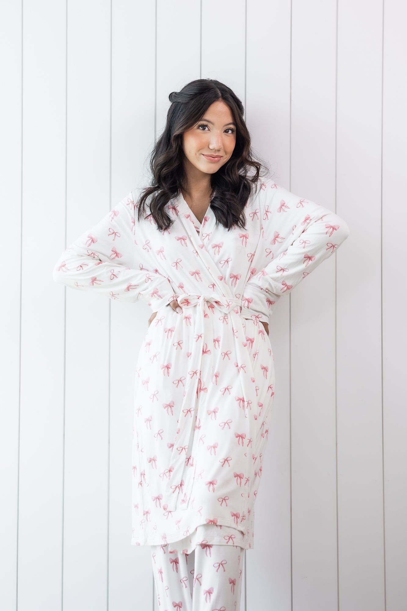 Woman wearing a white bow print robe against a white wooden panel background