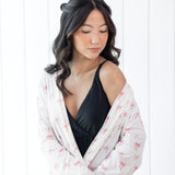 Woman wearing a black top and white bow print robe against a white background