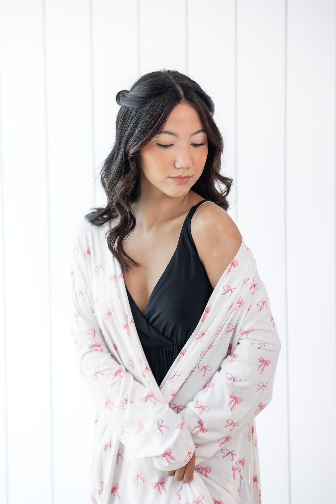 Woman wearing a black top and white bow print robe against a white background