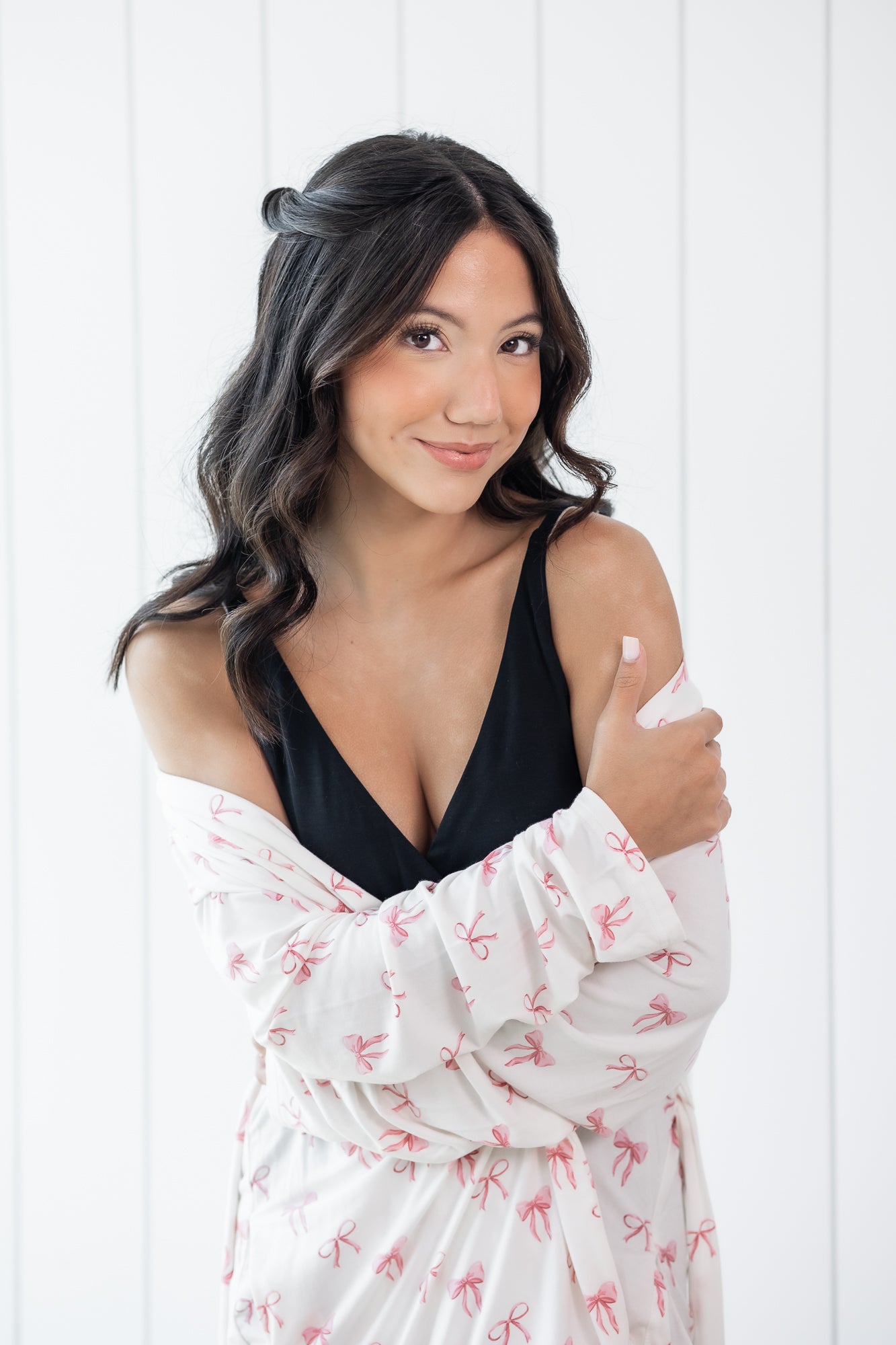 Woman wearing a black top and white pink bow robe against a white background