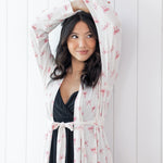 Woman wearing a sheer robe with pink bow pattern over a black outfit against a white background