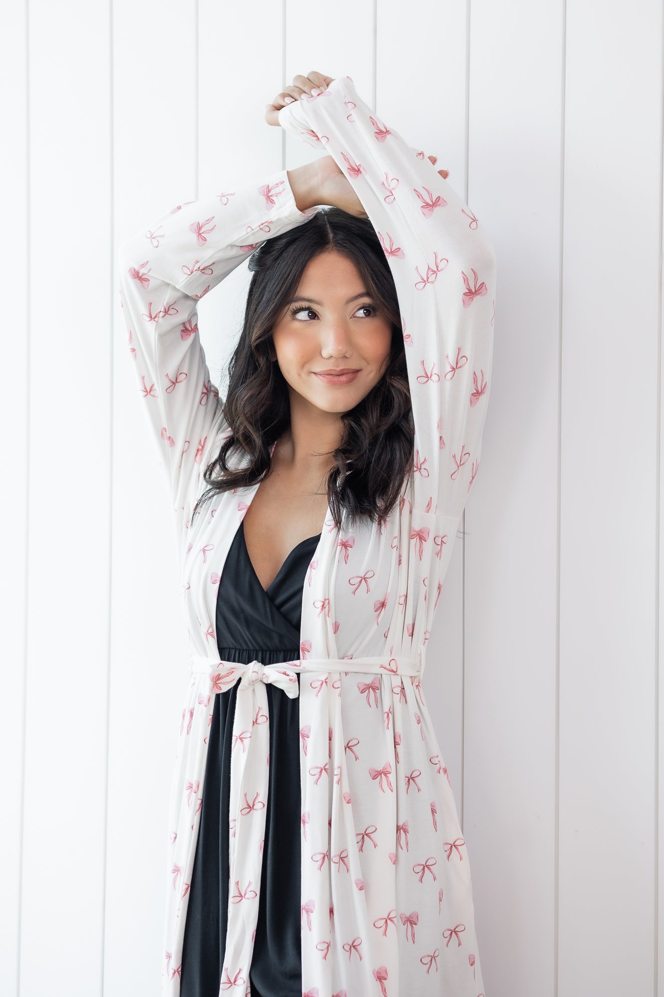 Woman wearing a sheer robe with pink bow pattern over a black outfit against a white background
