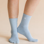 A pair of light blue ribbed crew socks worn on a person's feet, shown against a solid beige background.