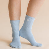 A pair of light blue ribbed crew socks worn on a person's feet, shown against a solid beige background.