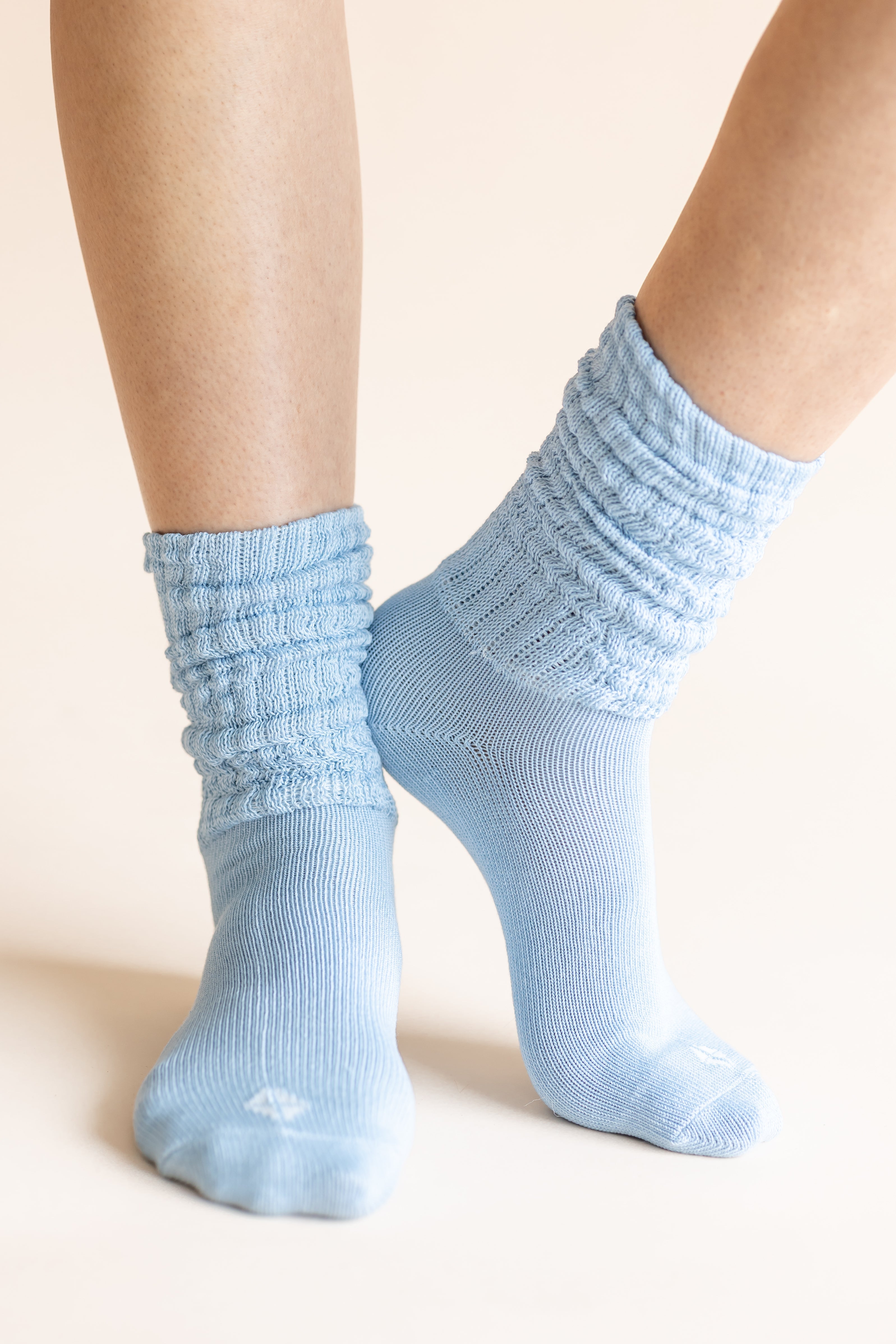 Light blue ribbed crew socks worn on a person's feet, shown against a plain warm beige background.
