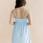 Woman wearing a light blue nightgown showing adjustable straps against a beige background