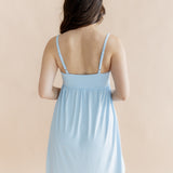 Woman wearing a light blue nightgown showing adjustable straps against a beige background