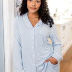 Woman wearing a light blue pajama set standing in a room with a white door and wooden floor.