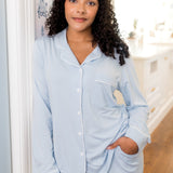 Woman wearing a light blue pajama set standing in a room with a white door and wooden floor.