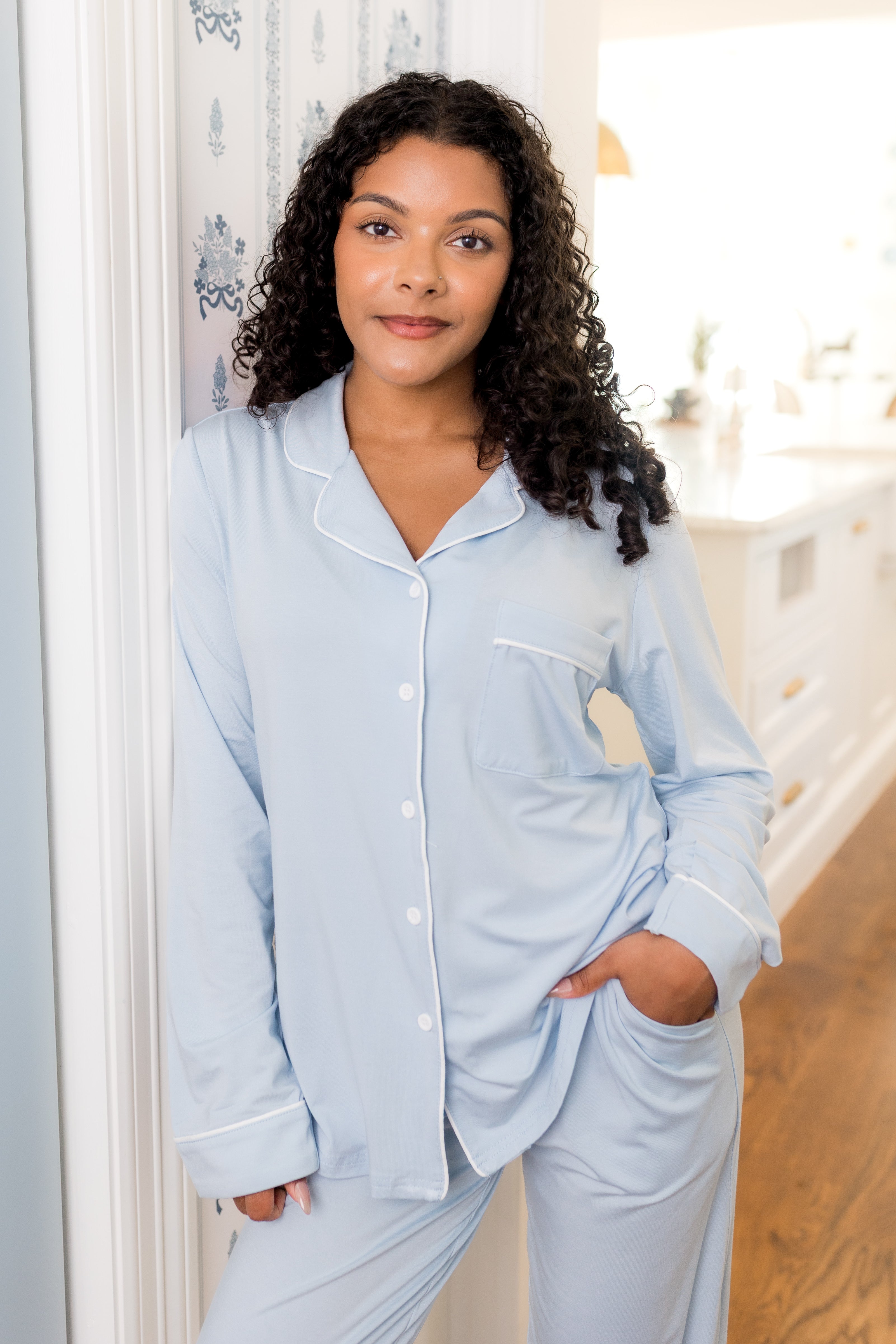 Woman wearing a light blue pajama set standing in a room with a white door and wooden floor.