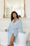 Woman in a light blue robe sitting on a white tub in a bathroom. ::: Model is 5'0" wearing size XS/S ///
