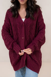 Person wearing a burgundy knitted cardigan against a plain background