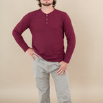 Male model with one hand on hips while wearing Kyte Long Sleeve Henley Tee in Burgundy paired with tan pants 