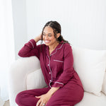 Smiling model sitting on a white couch while wearing Women's Long Sleeve Pajama Set in Burgundy