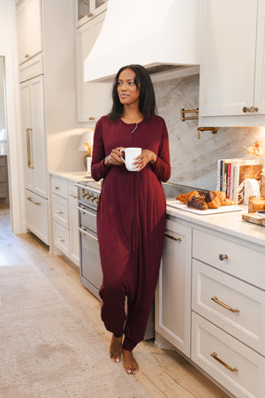 Model wearing Adult Sleep Sack in Burgundy standing in kitchen holding mug