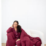 Model looking to the side while sitting on a white sofa chair wrapped in a Quilt Blanket in Burgundy 2.5 