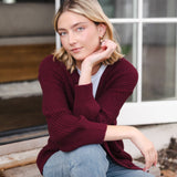 Modal posing outdoors wearing Chunky Knit Women's Waffle Cardigan in Burgundy over white t-shirt and blue jeans