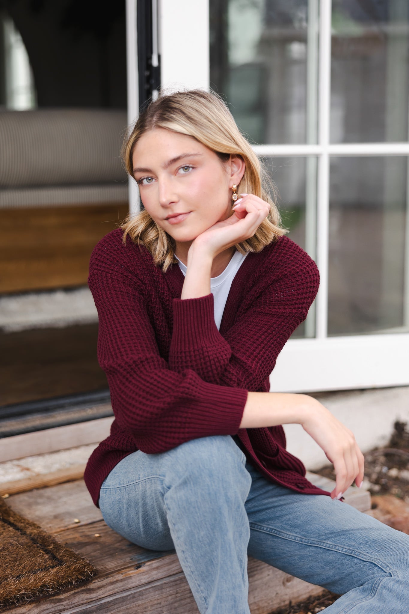Modal posing outdoors wearing Chunky Knit Women's Waffle Cardigan in Burgundy over white t-shirt and blue jeans