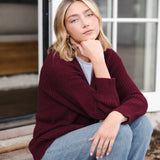 Modal sitting outdoors wearing Chunky Knit Women's Waffle Cardigan in Burgundy over white t-shirt and blue jeans
