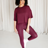 Female standing on one foot with the other foot resting against her leg wearing the Bamboo Flex Women’s Leggings in Burgundy and matching short sleeve tee