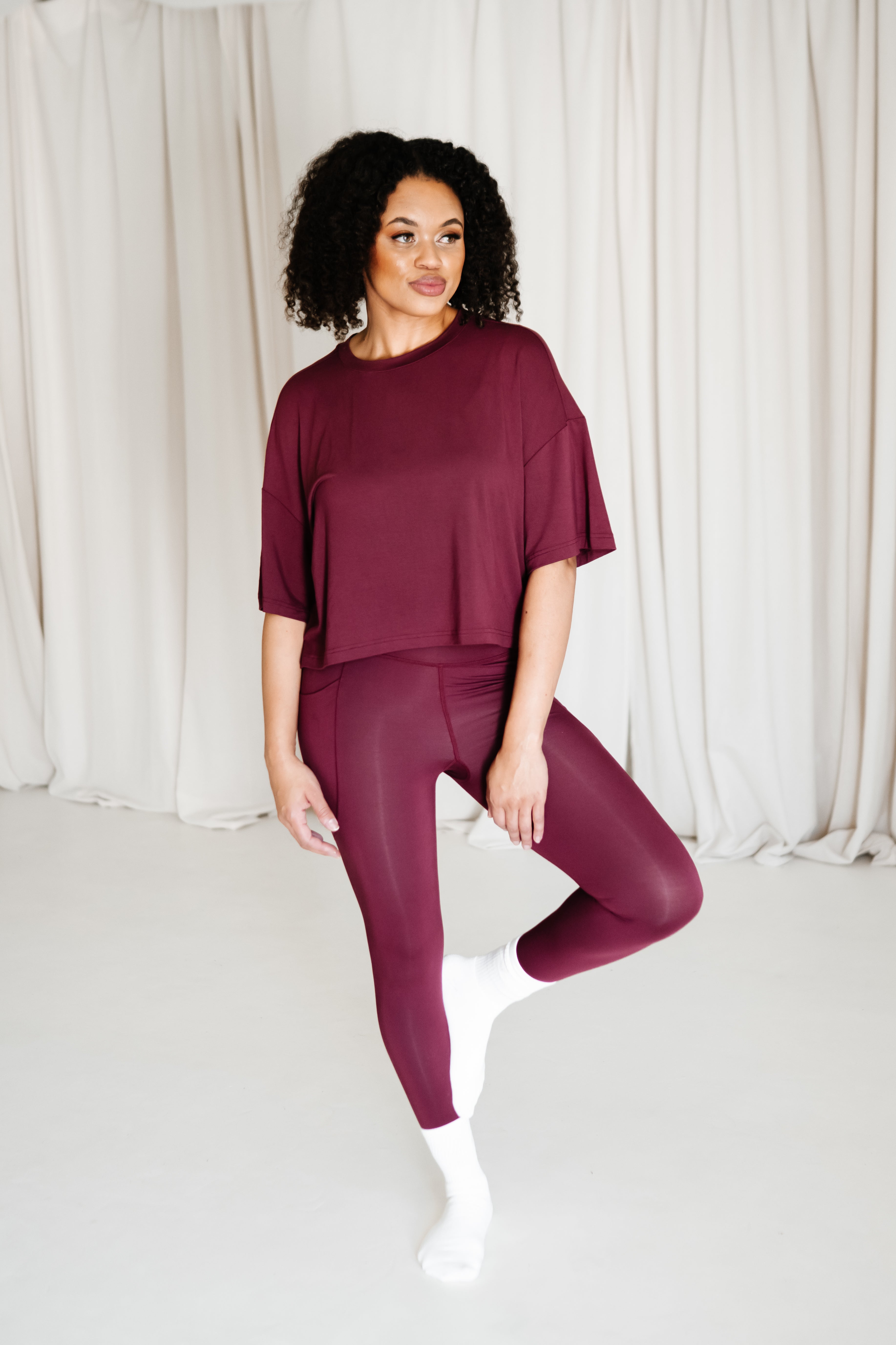 Female standing on one foot with the other foot resting against her leg wearing the Bamboo Flex Women’s Leggings in Burgundy and matching short sleeve tee