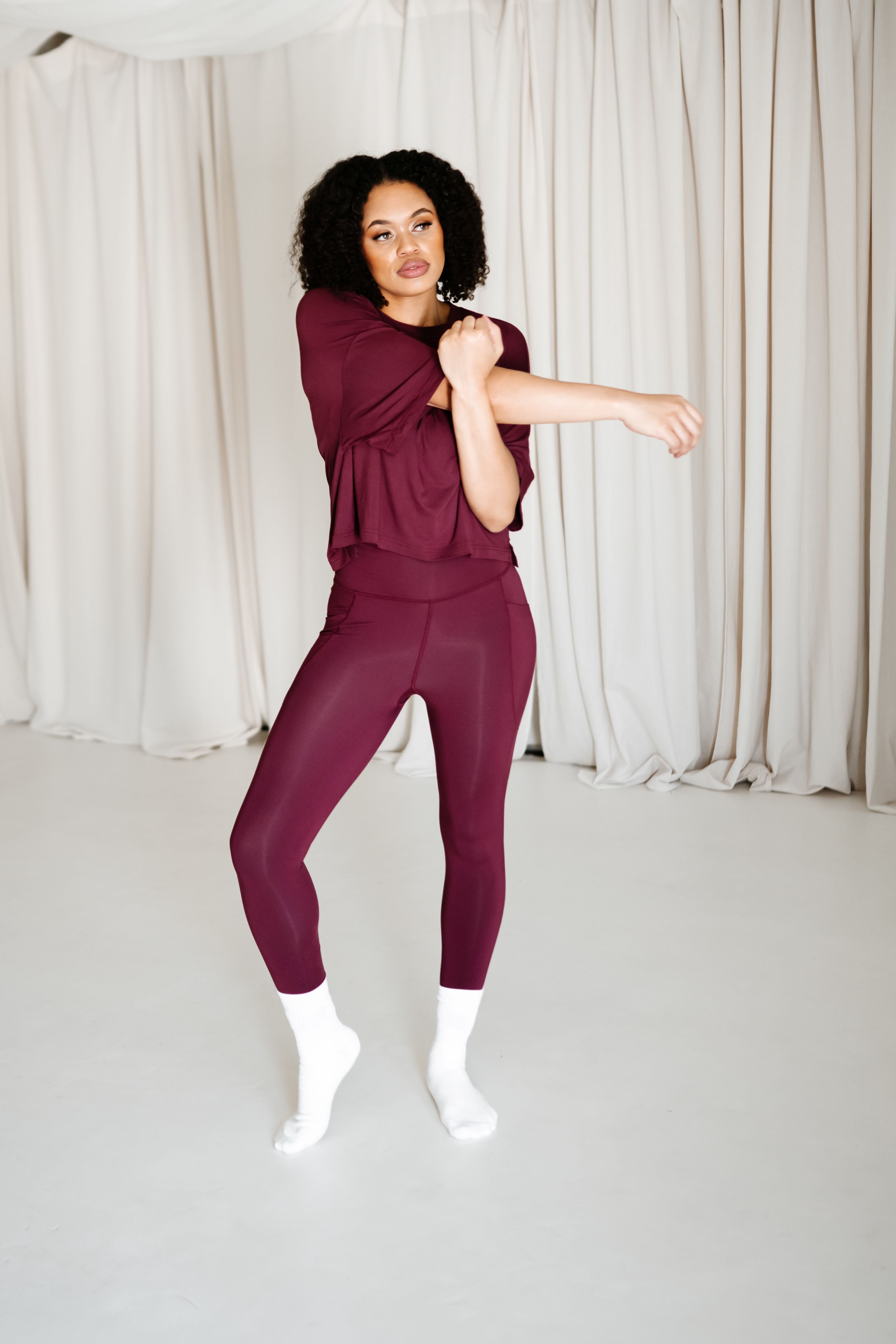 Female model stretching wearing the Bamboo Flex Women’s Leggings in Burgundy and matching short sleeve tee