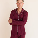 Model wearing Men's Long Sleeve Pajama Set in Burgundy standing with folded hands on a beige background
