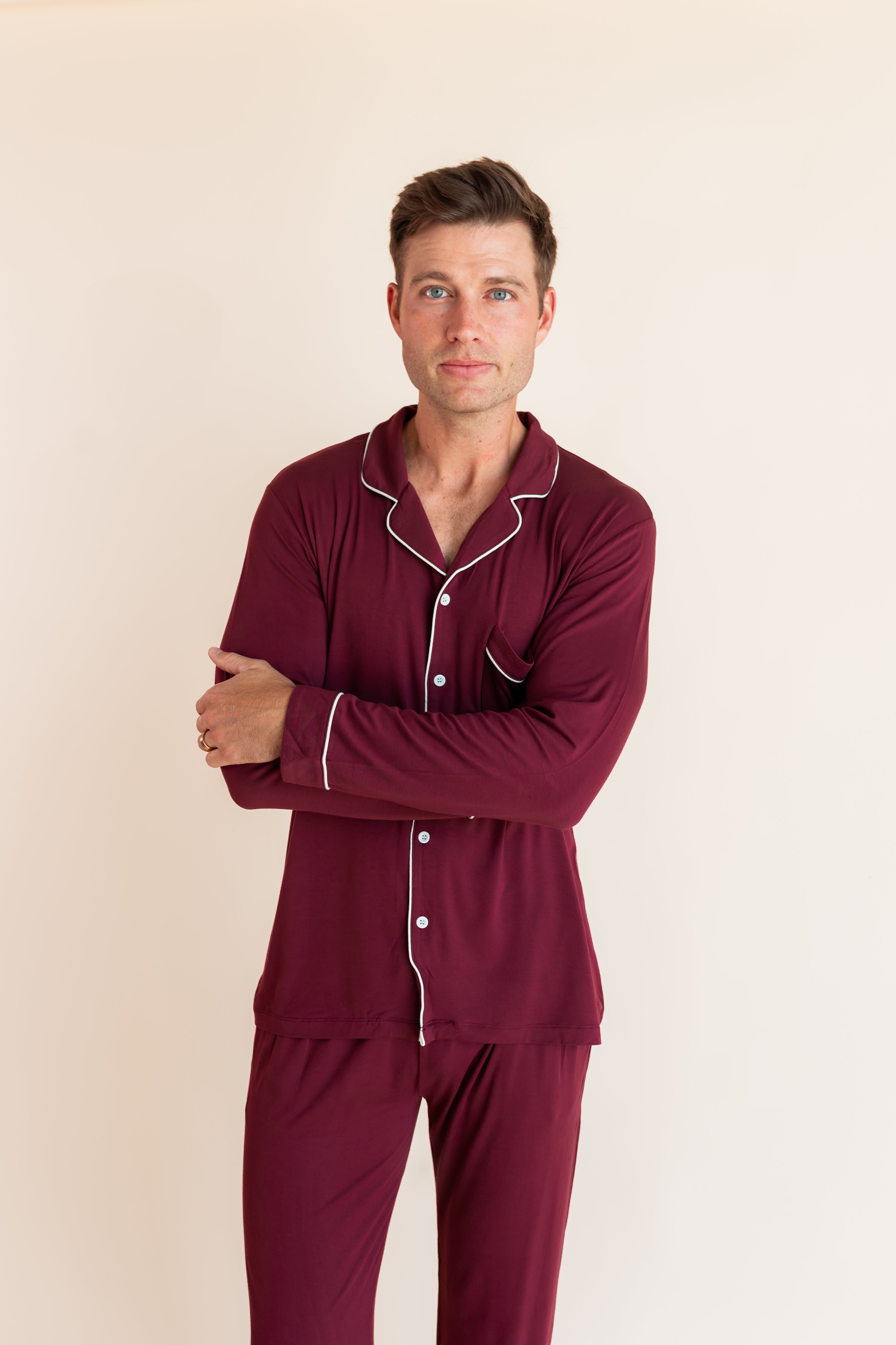 Model wearing Men's Long Sleeve Pajama Set in Burgundy standing with folded hands on a beige background