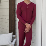 Male model leaning against a white house wearing the Men's Ribbed Henley Set in Burgundy