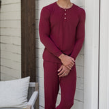 Male model leaning against a white house wearing the Men's Ribbed Henley Set in Burgundy