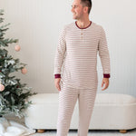 Male smiling looking off to the side standing in front of a cream ottoman and two decorated Christmas trees wearing the Men's Ribbed Henley Set in Burgundy Stripe