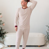 Male model standing in front of a cream ottoman between two christmas trees wearing the Men's Ribbed Henley Set in Burgundy Stripe with one hand behind his head